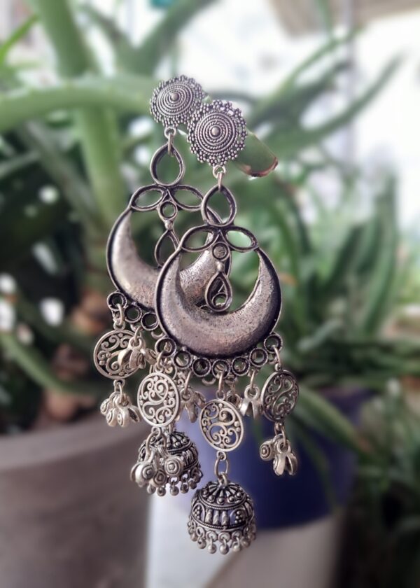 Large oxidised earrings with intricate detailing, featuring a textured circular stud, crescent moon design, and dangling jhumkas.