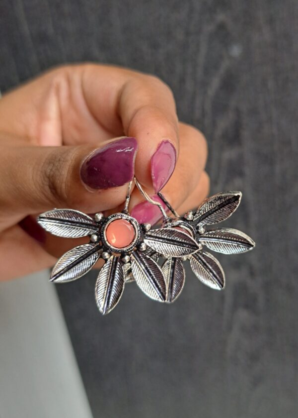 Pink oxidised earrings with intricate floral patterns and a soft pink stone, showcasing a vintage silver finish.