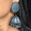 black oxidised jhumka earrings with intricate circular tops and dangling bell-shaped charms.