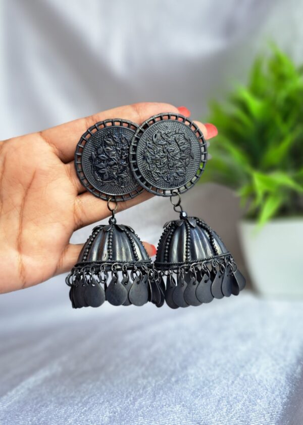 black oxidised jhumka earrings with intricate circular tops and dangling bell-shaped charms.